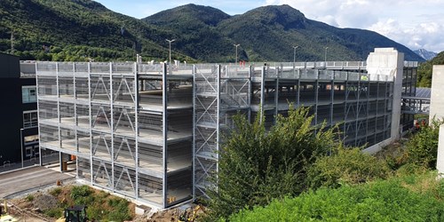 Steel multi-storey parking garage with mountains in the background and green bushes in the foreground